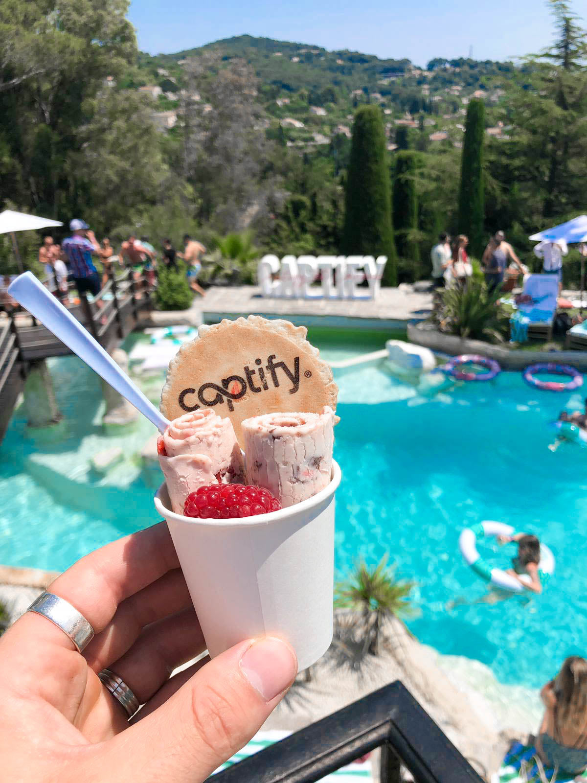 Cup of pink ice cream rolls topped with fruit and a Captify branded wafer beside an outdoor pool